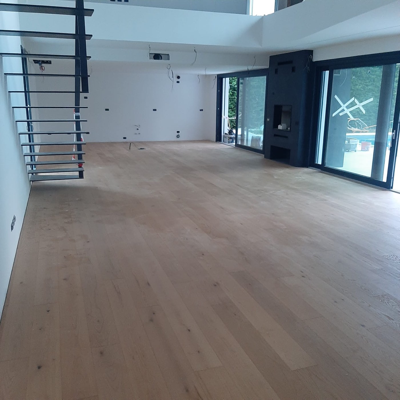Soggiorno open space a doppia altezza con pavimento in legno, camino e vista sulla piscina