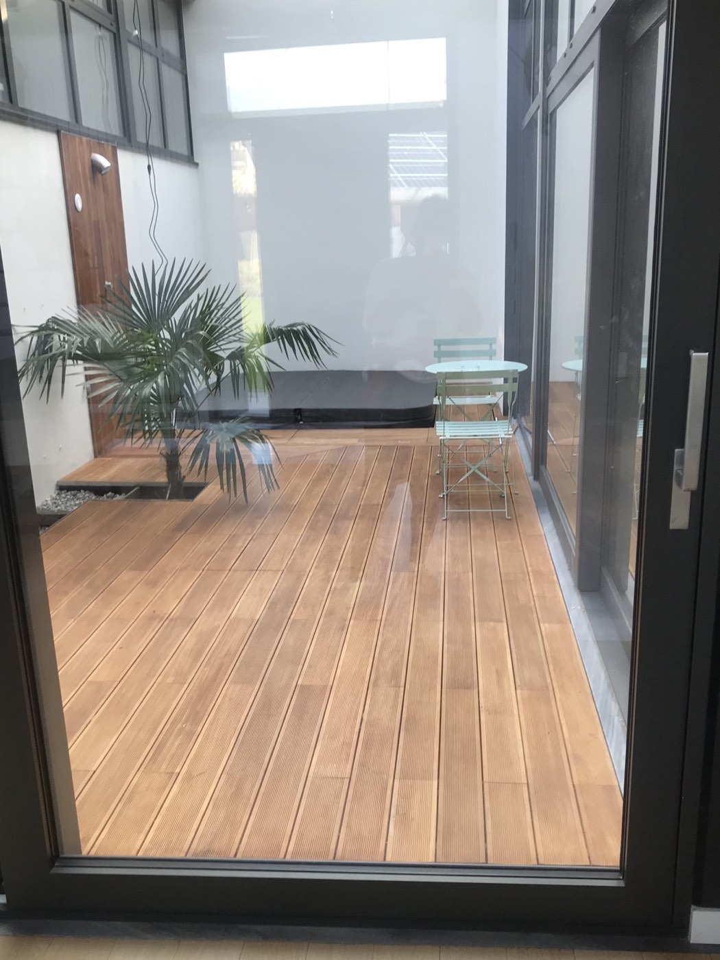 Cortile interno con pavimentazione in legno e arredo da esterno visto da una porta vetrata